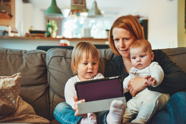 A mother is holding her two babies while researching tips for family healing post-divorce on her tablet.